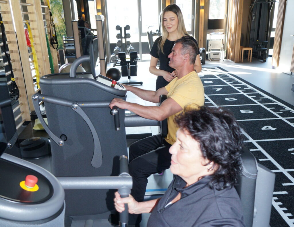 Mehrere Patient*innen trainieren den Rücken unter Aufsicht einer Trainerin