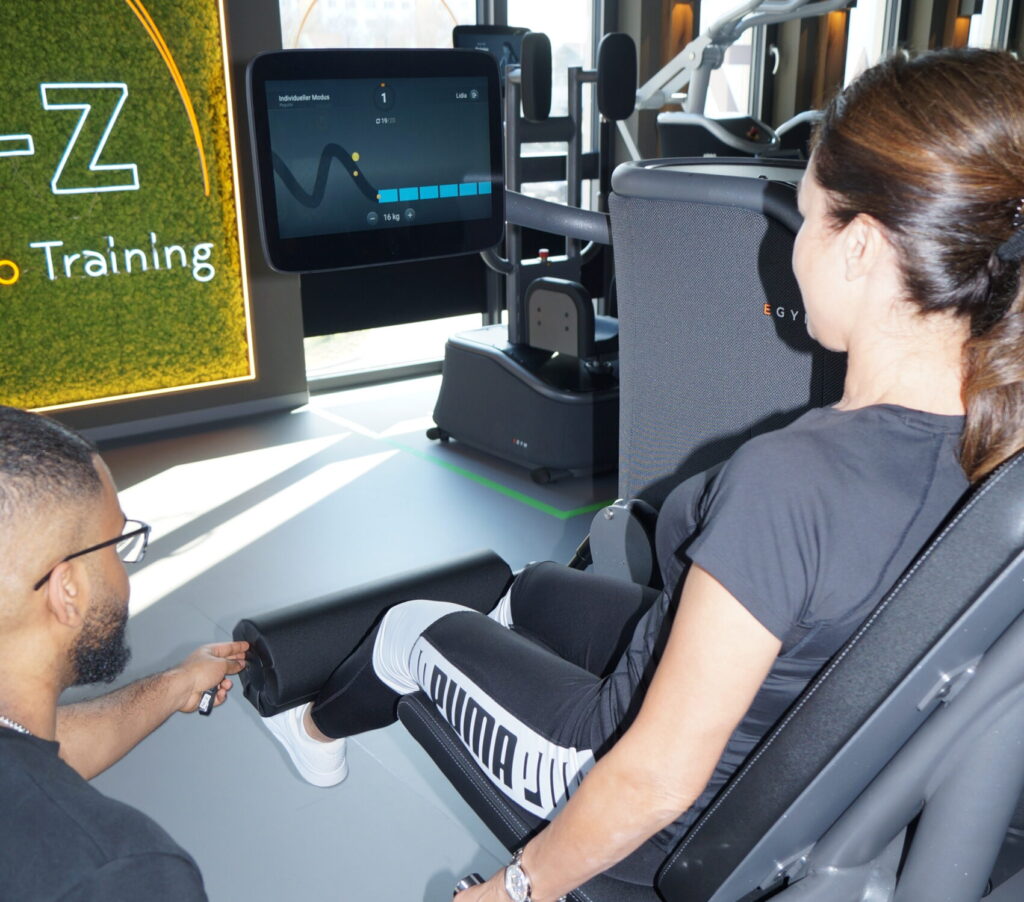 Trainer mit Patientin an modernem Trainingsgerät